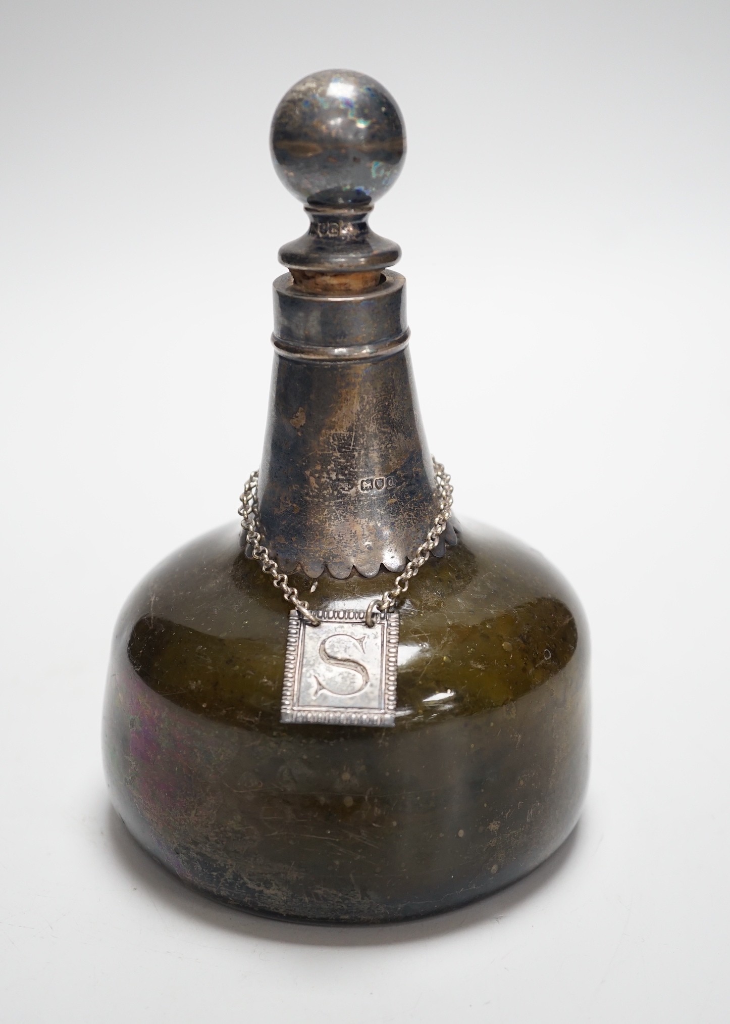 An 18th century green glass onion-shape bottle, with later silver mount, London, 1899, together with a George III silver 'S' decanter label, Phipps & Robinson, London, 1806. 17cm